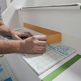 A person applying carpet adhesive tape to a stair riser