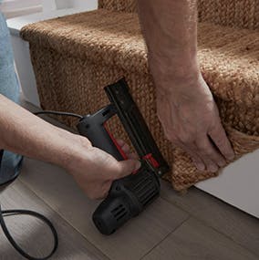 A person stapling the stair runner to the final stair riser