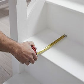 A person measuring the depth of a stair tread with a tape measure