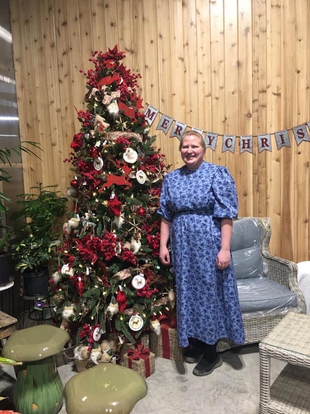 Smiling lady in blue dress standing beside Christmas tree