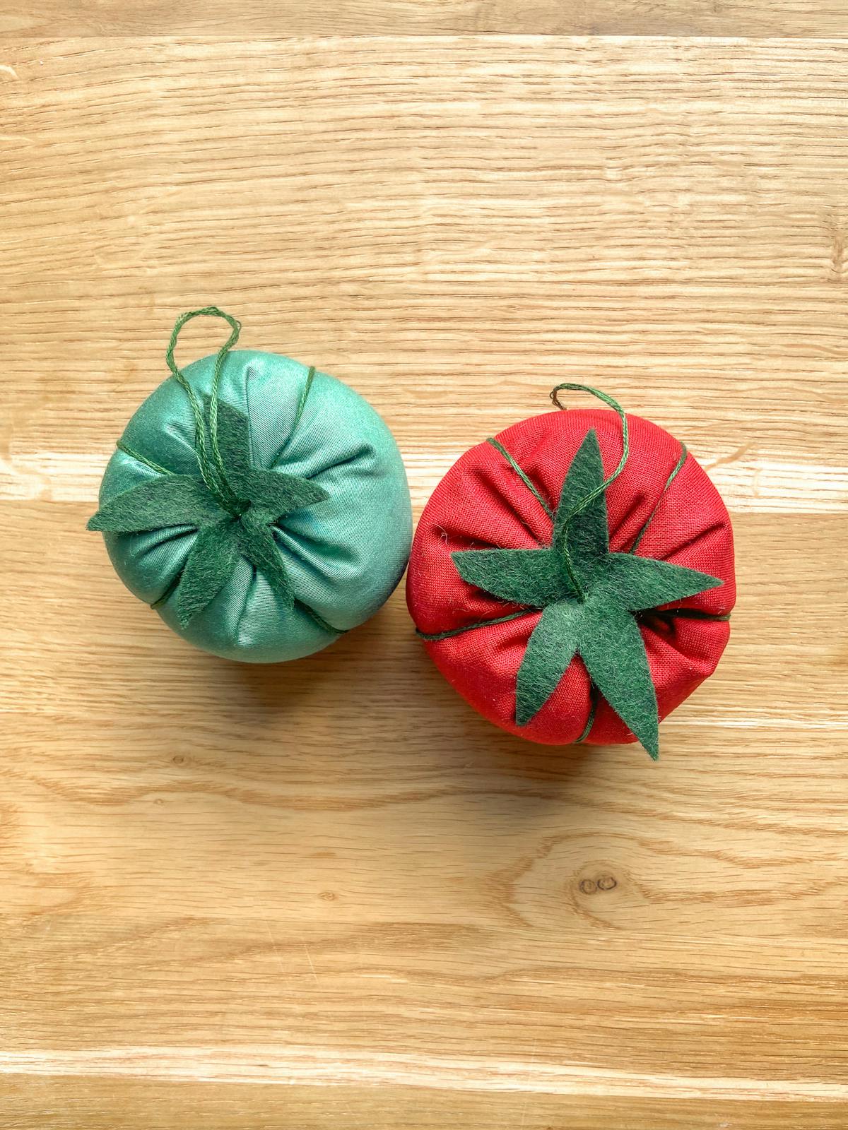  Afgewerkte tomaatvormige speldenkussens in groen en rood op een houten tafel