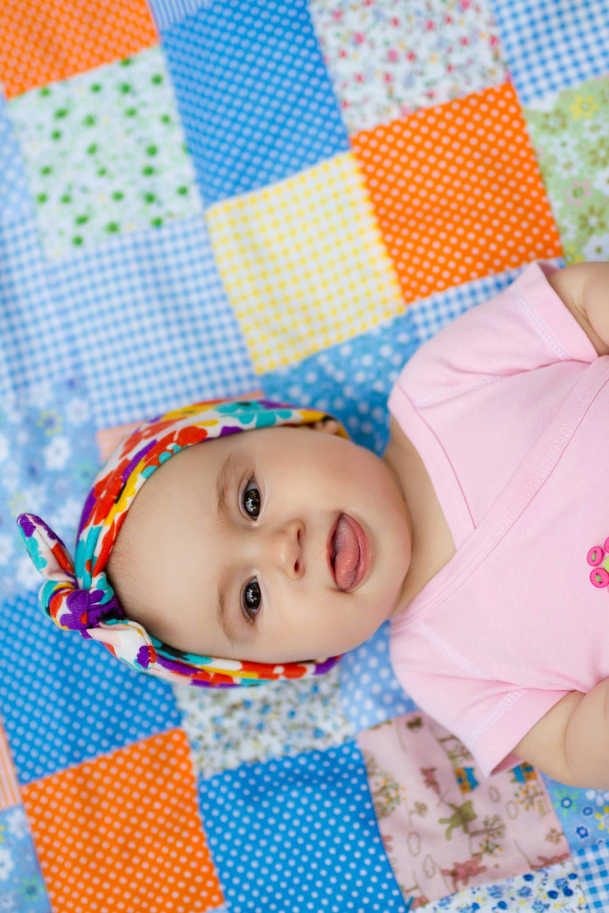  smiling baby lying on top of colourful quilt