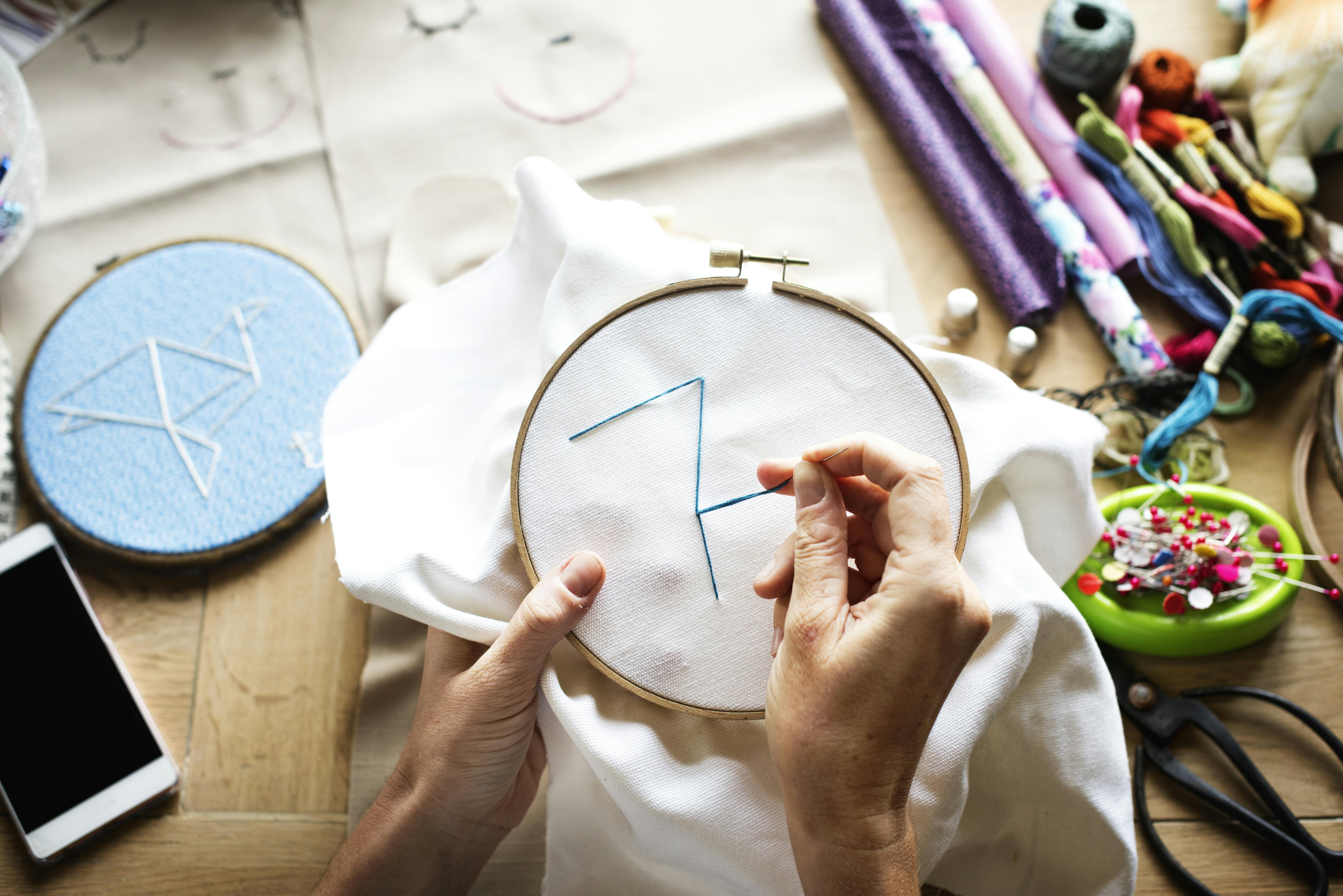  hands embroidering pattern using embroidery hoop with supplies in background