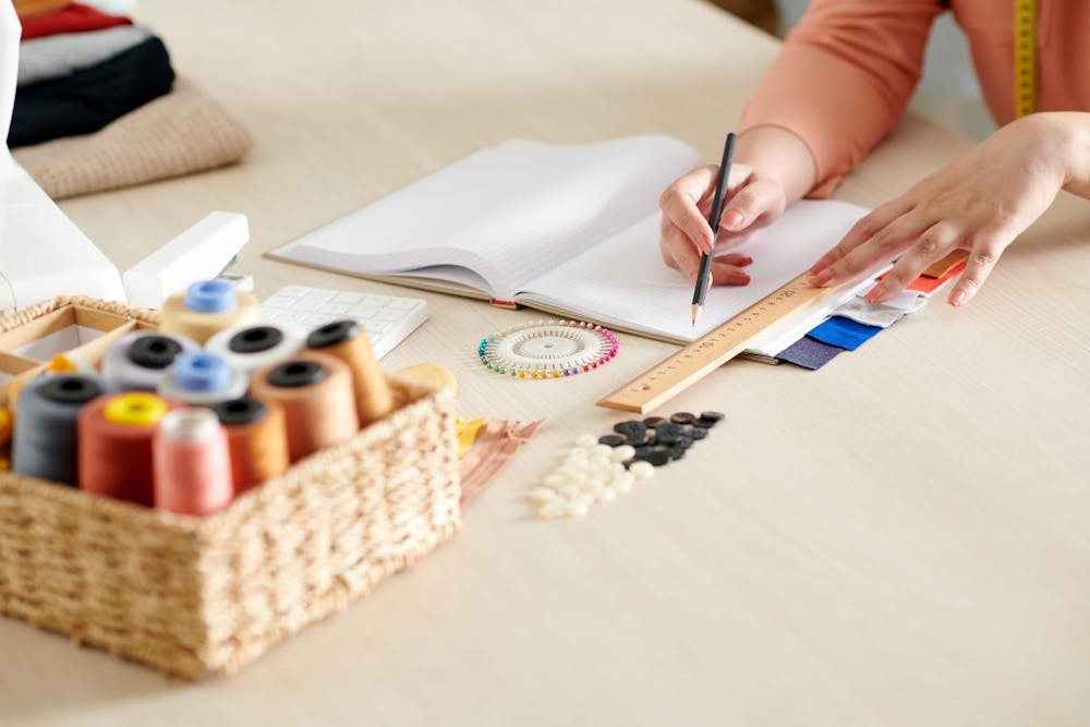  primer plano de la mesa de un estudio de costura con hilos de colores, alfileres y una libreta