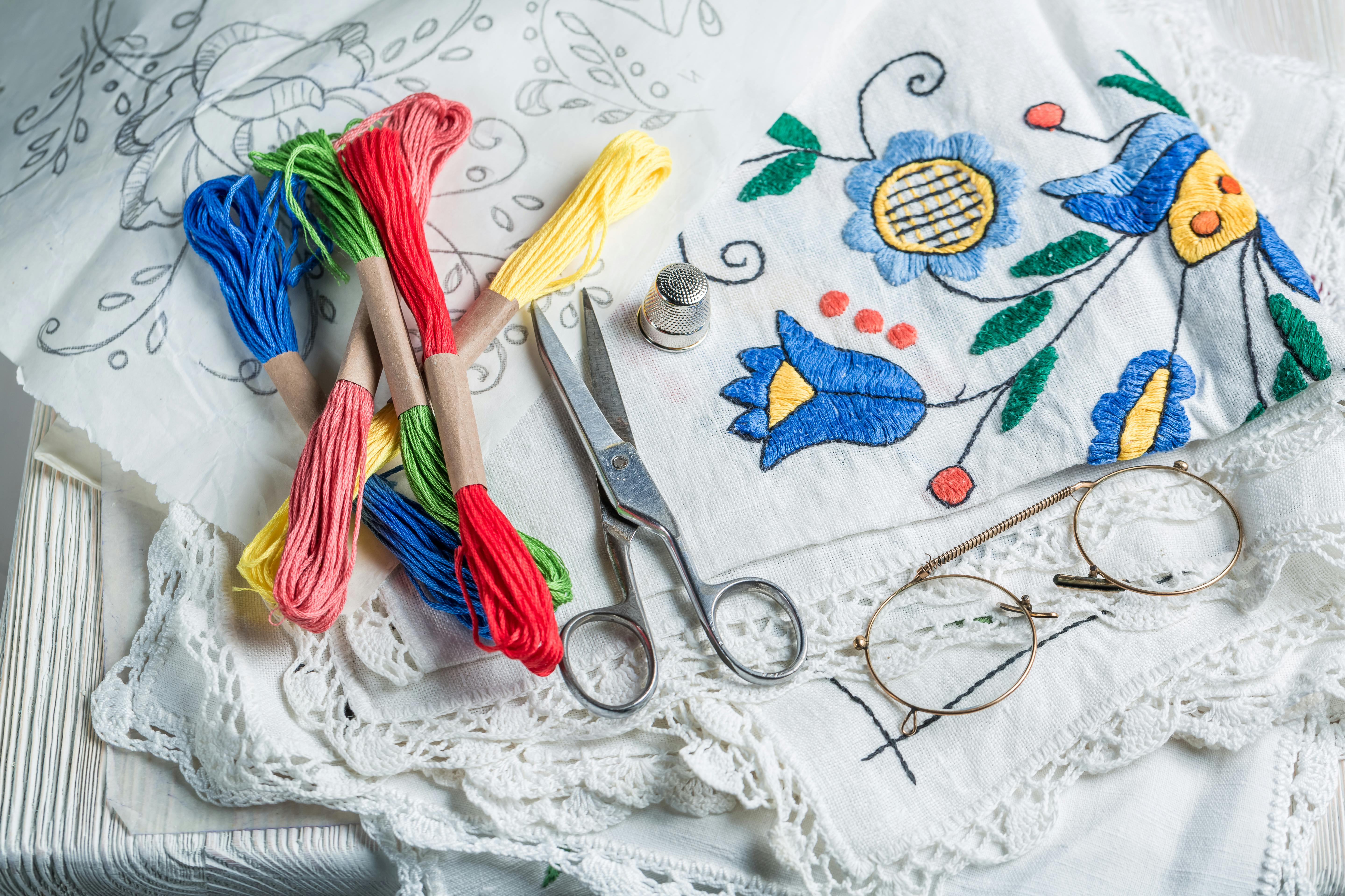  photo of embroidery supplies like threads, scissors, thimble, needles and a pattern