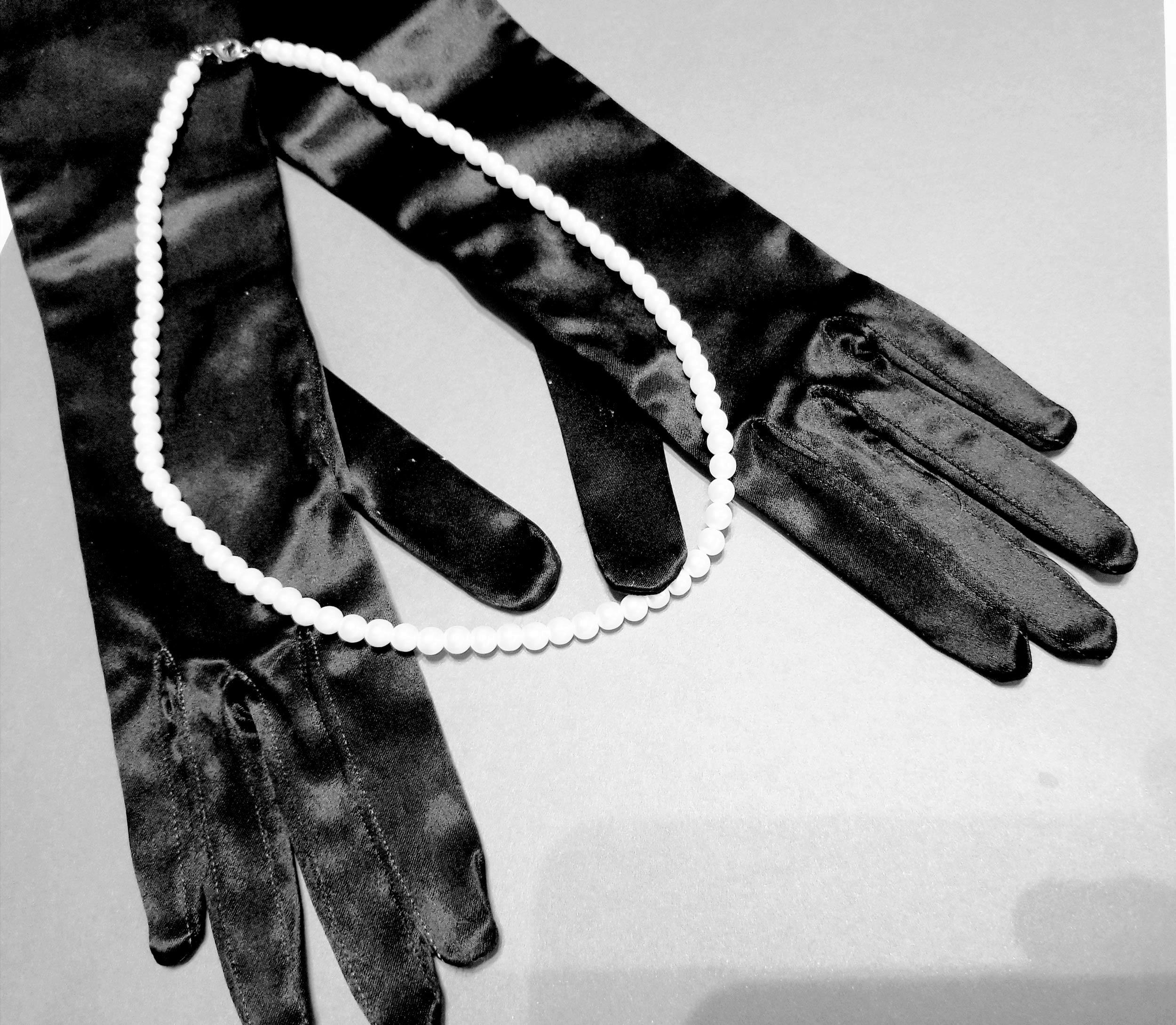 close up black and white photo of satin gloves and pearls