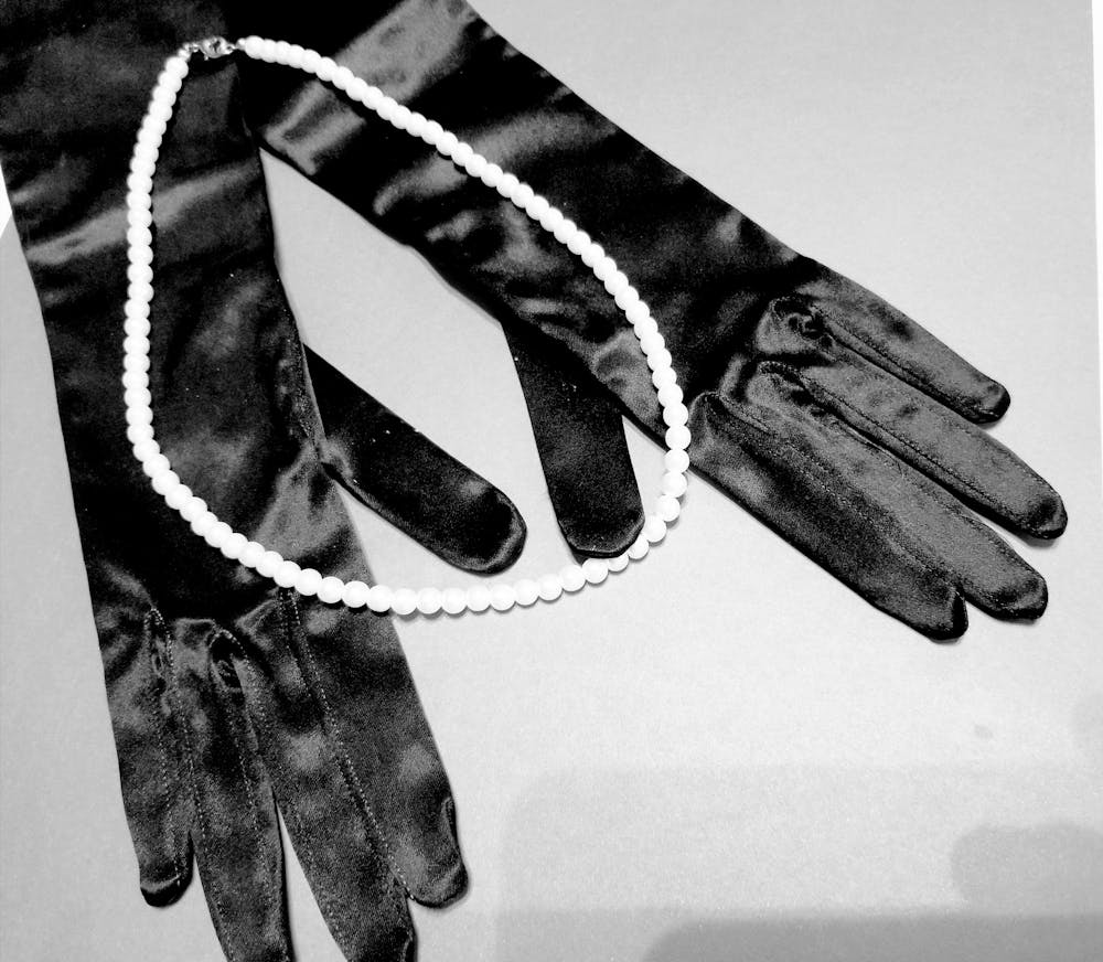  close up black and white photo of satin gloves and pearls