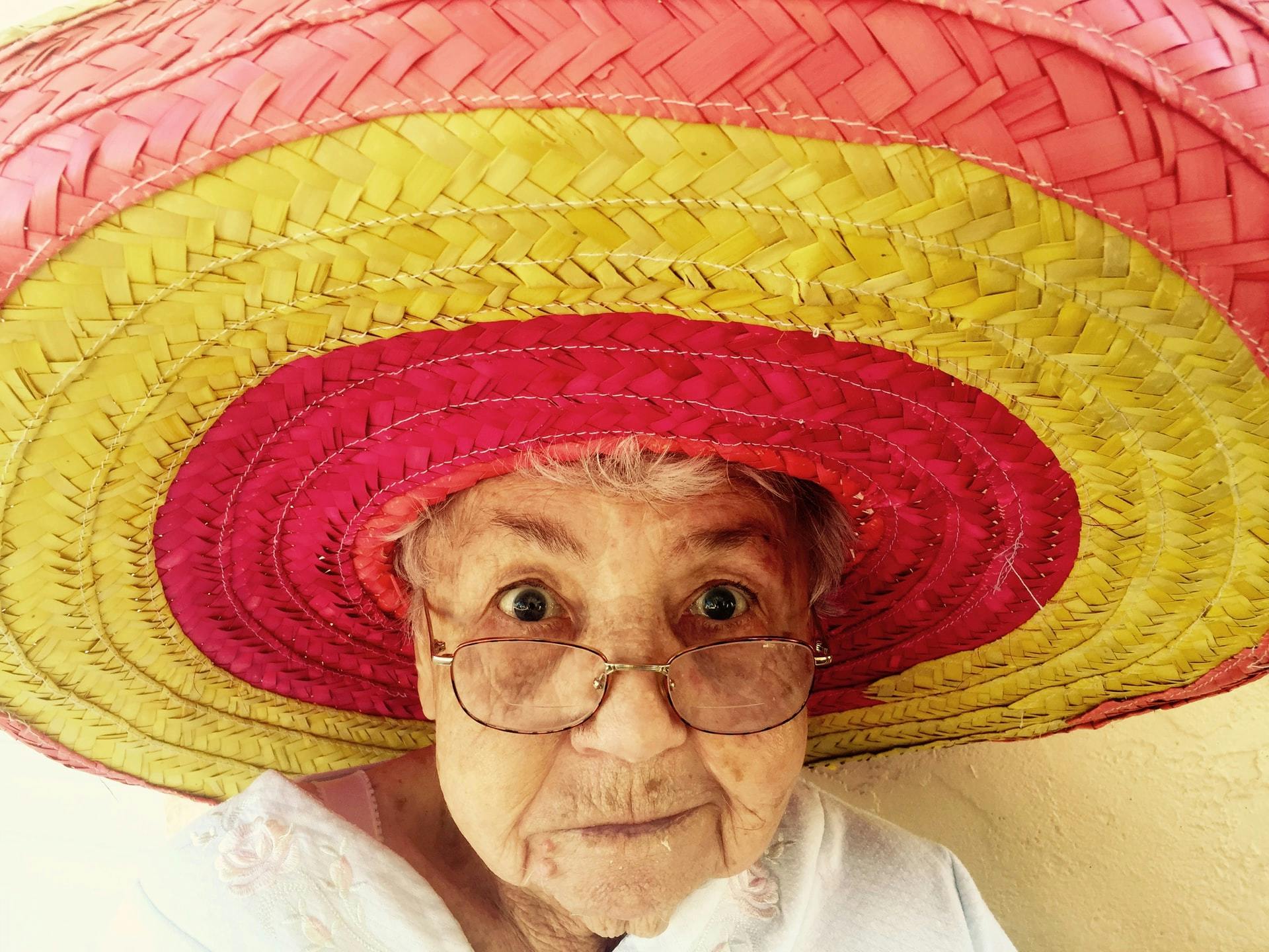 Oude vrouw met een felgekleurde sombrero die naar de camera kijkt