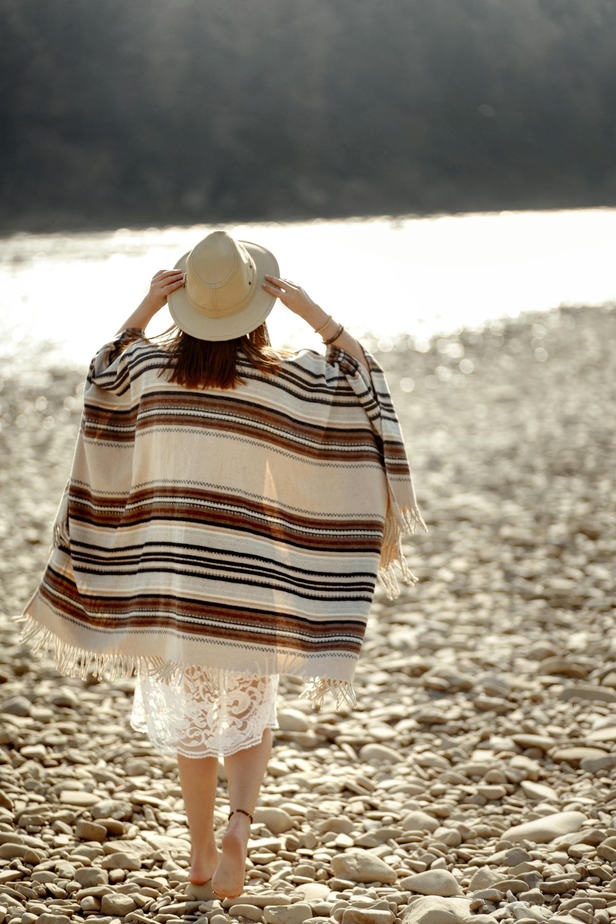  woman walking along the beach in beach poncho and hat