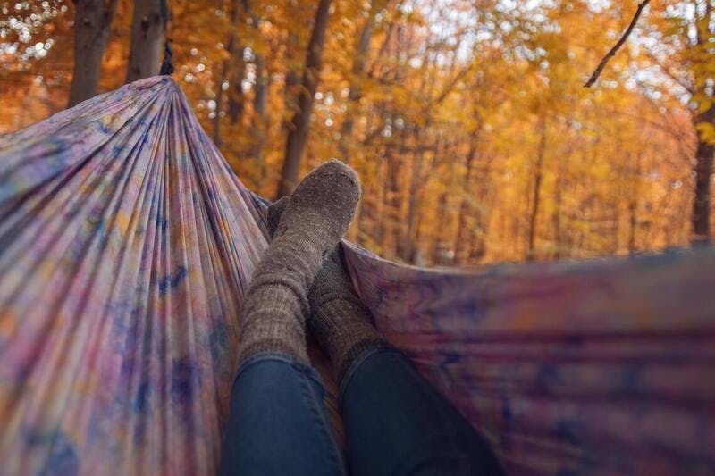 person lounging on a tie dyed hammock in the woods