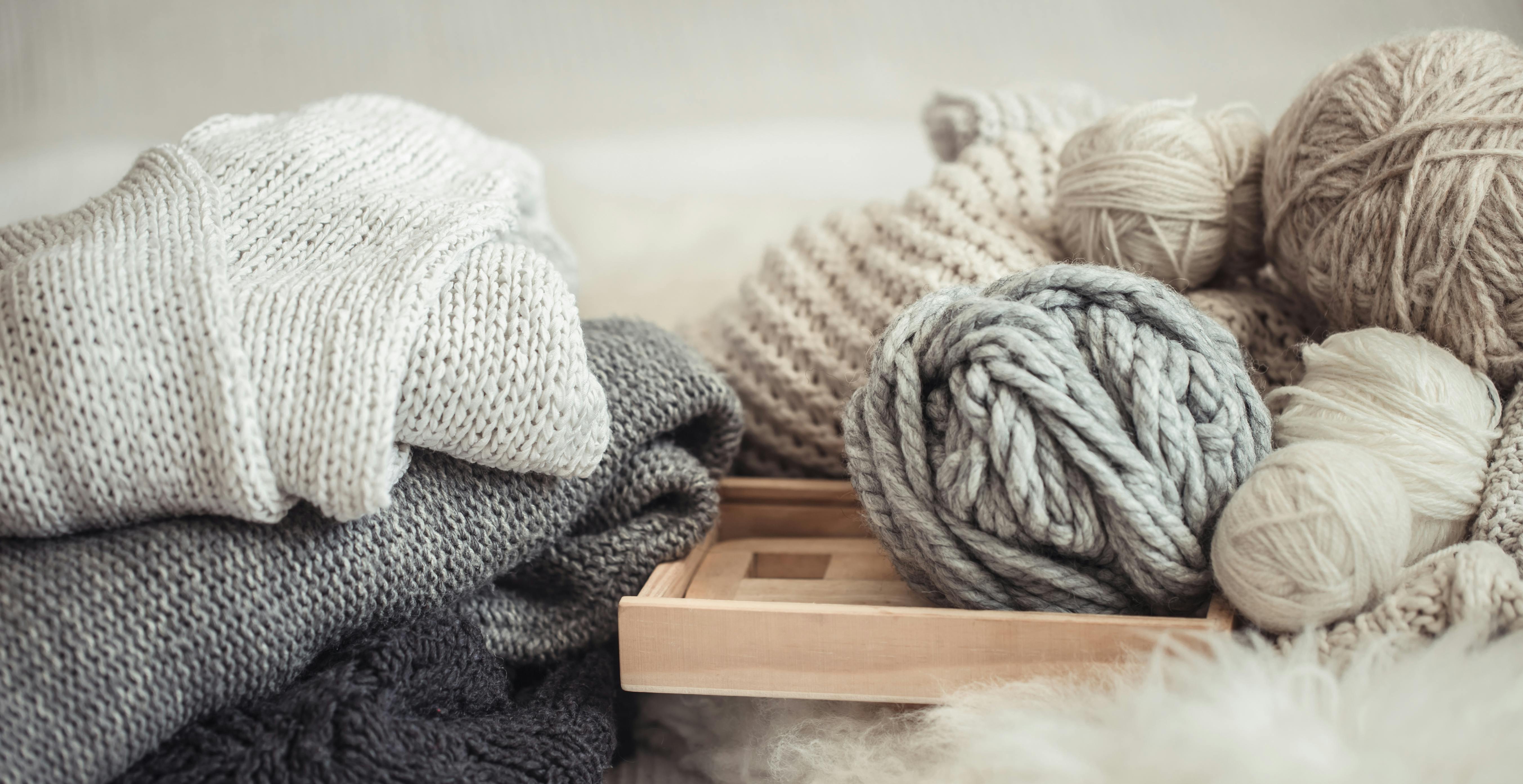  textured yarn and knitted clothing in a pile on a wooden board