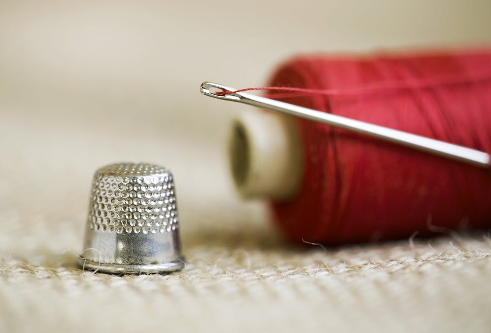 close up photograph of needle, red thread and thimble