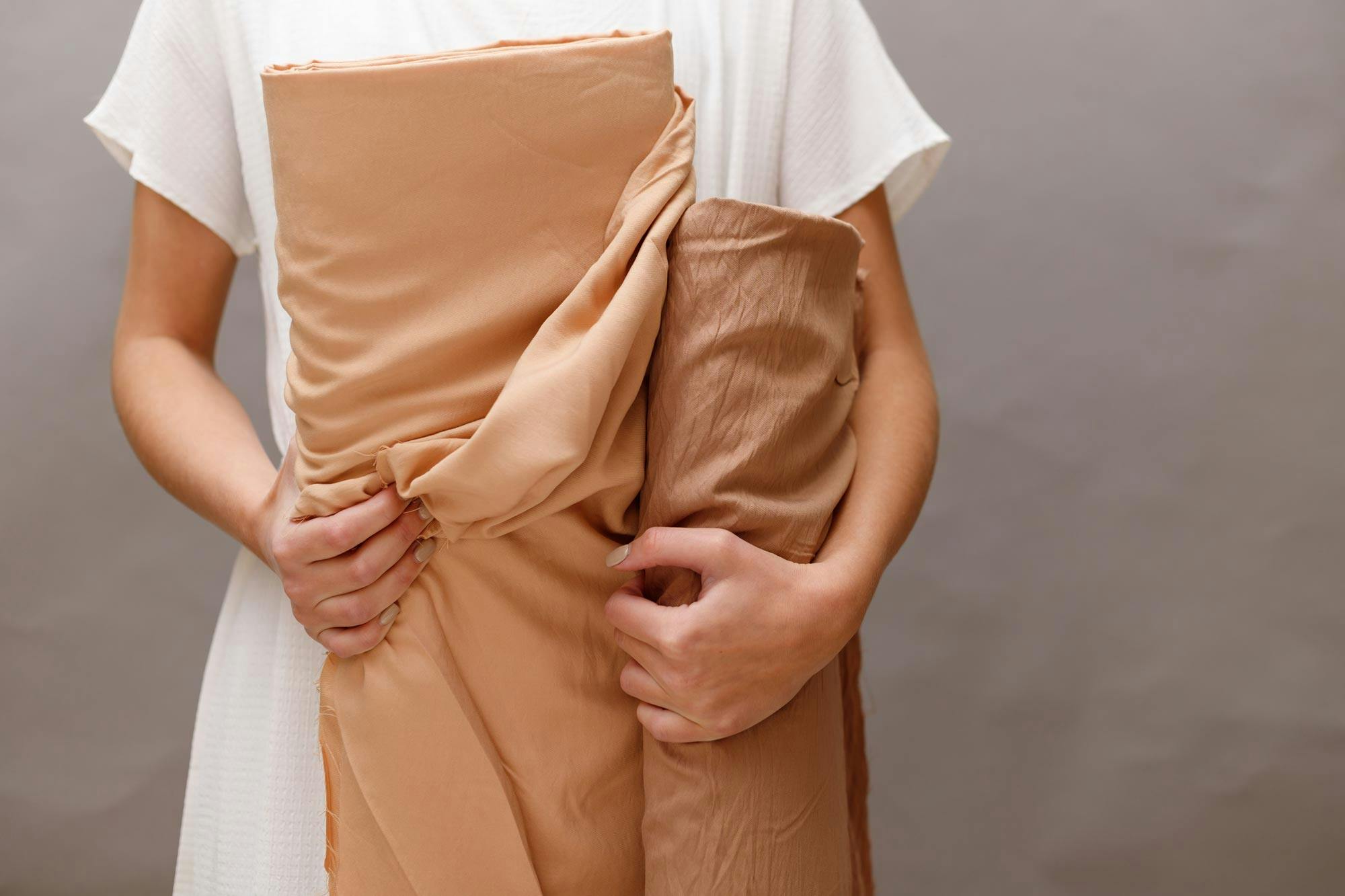  woman holding two rolls of peach coloured fabric