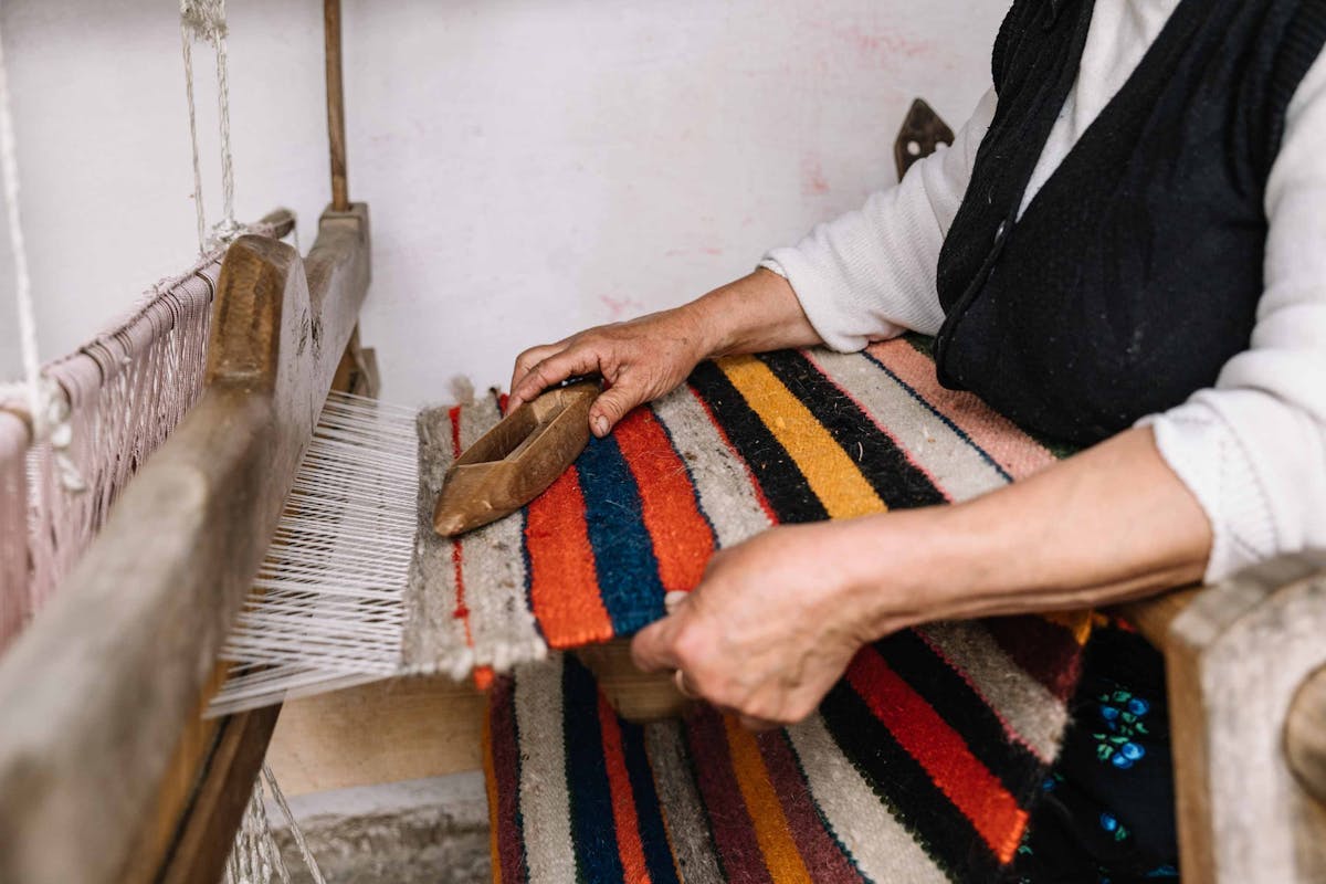  woman weaving brightly colored carpet at a traditional loom