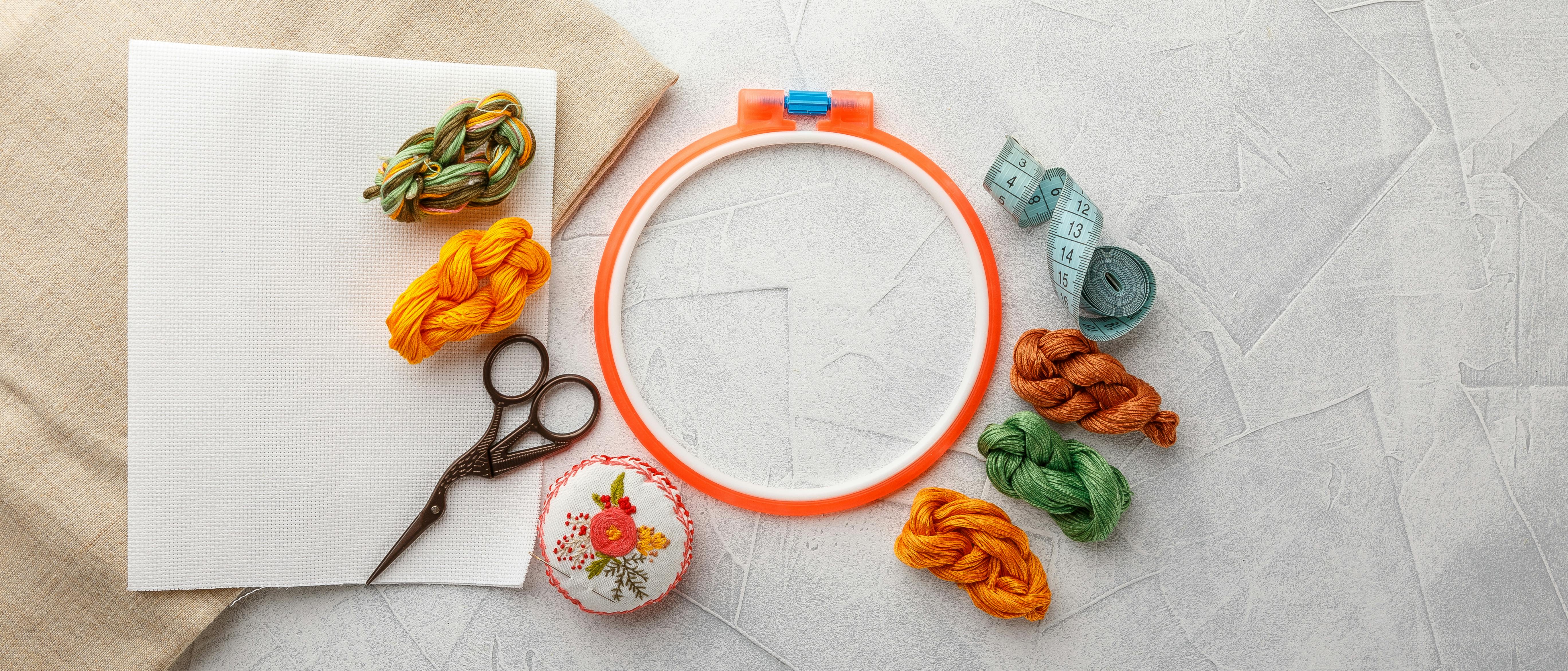 an embroidery hoop with scissors, fabric and threads around the outside