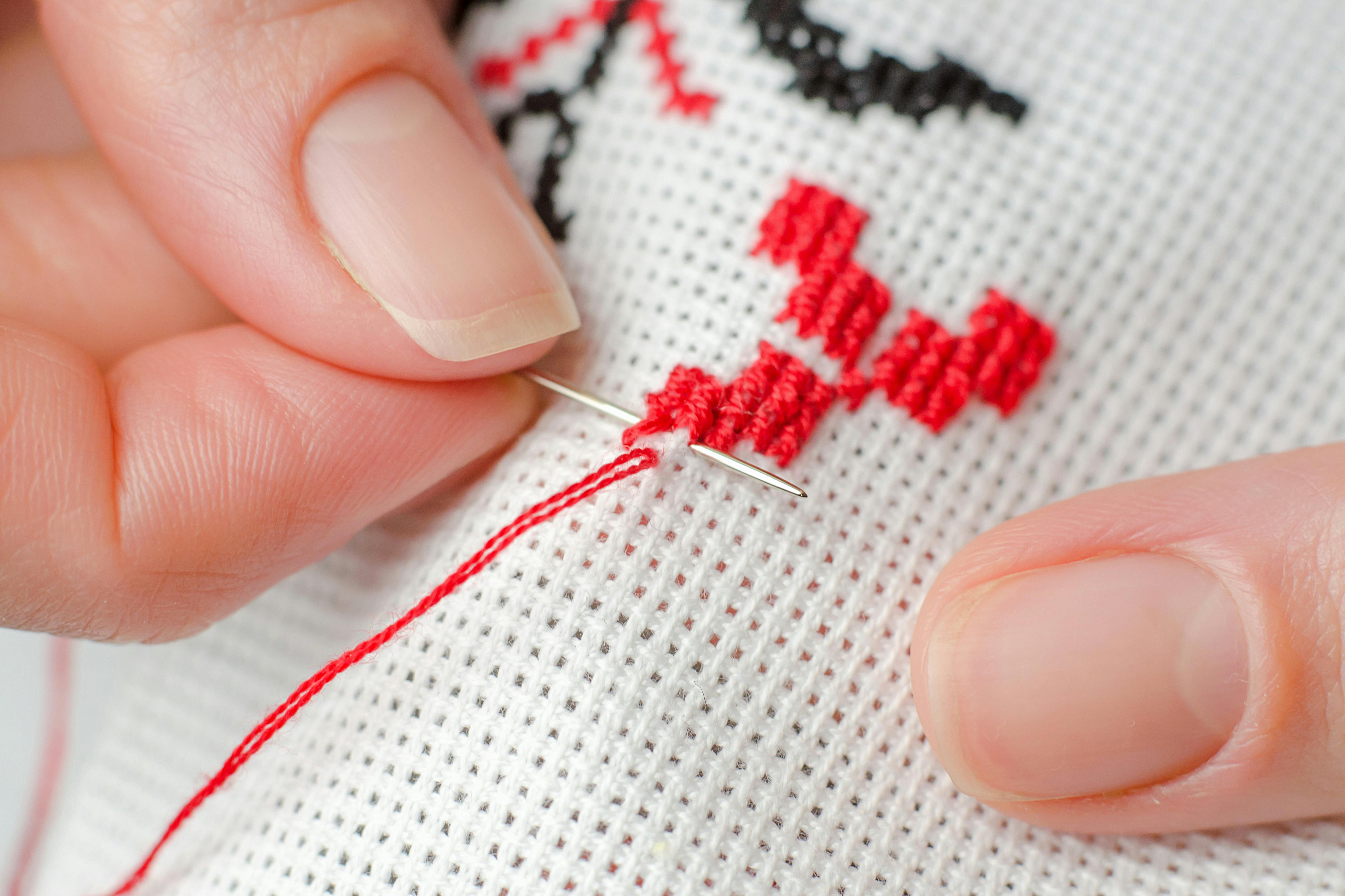  close up of hands embroidering red emblems