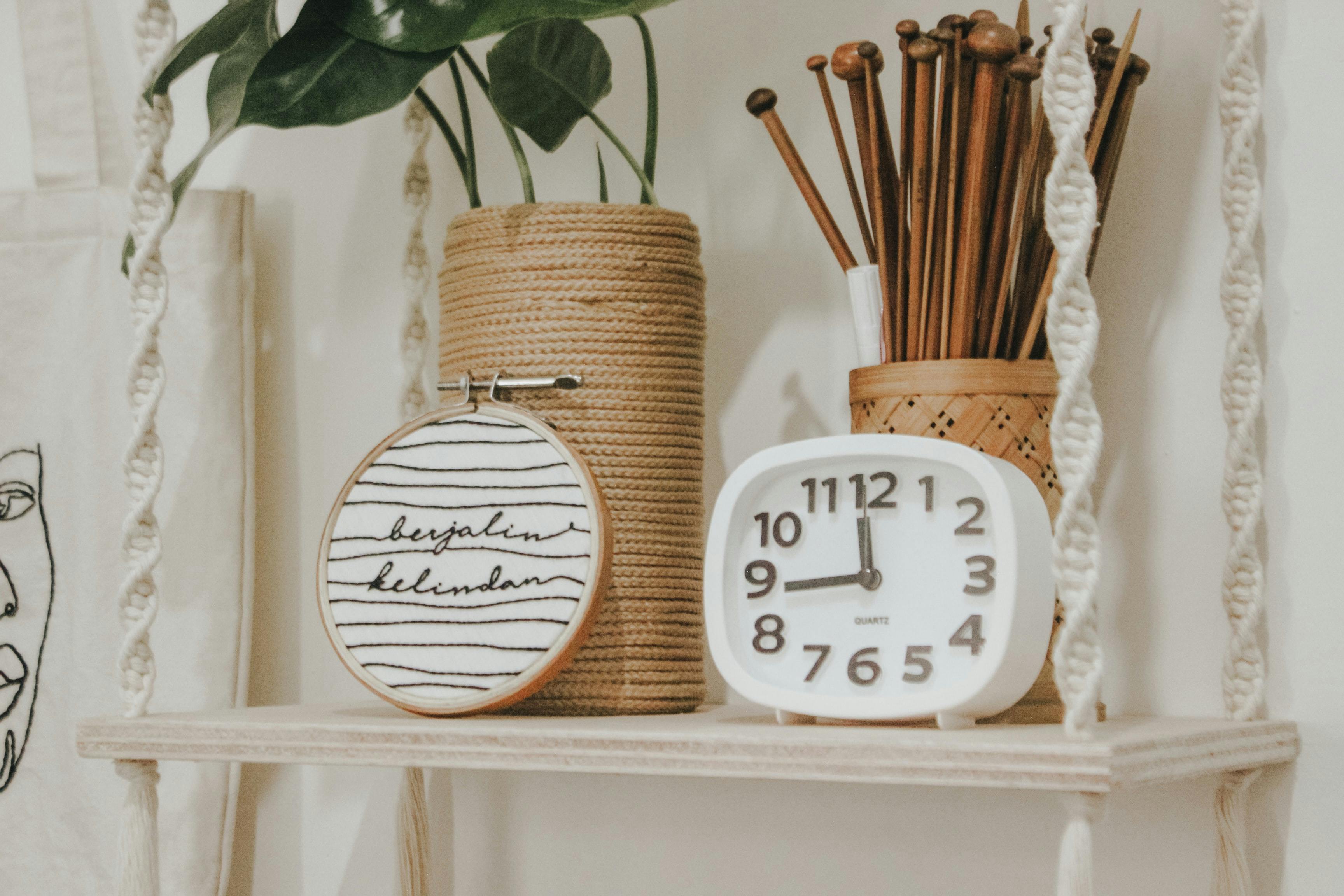  A macrame shelf holding a plant, sewing project, and an alarm clock.