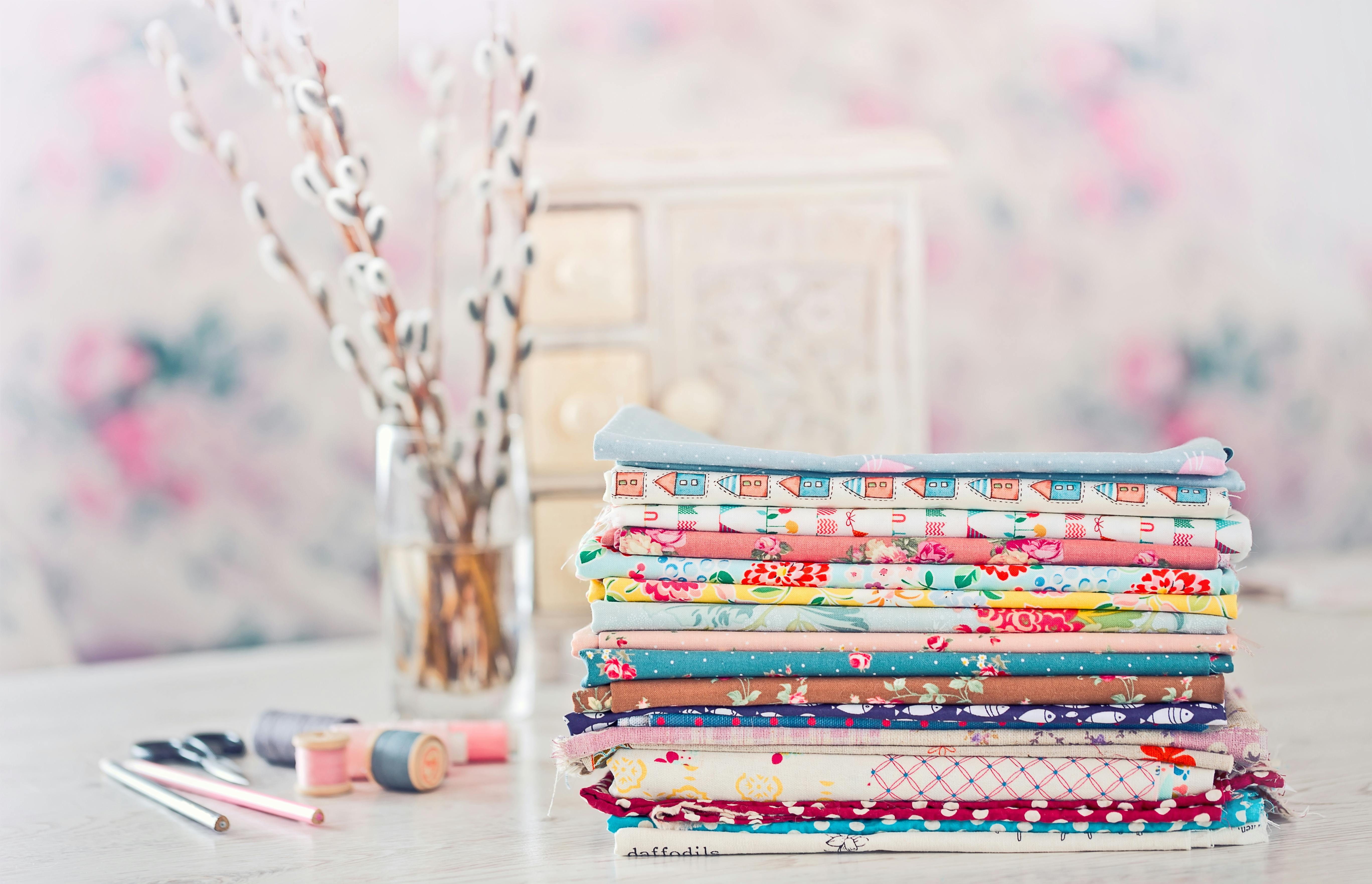 stack of quilting cottons against pastel background and vase