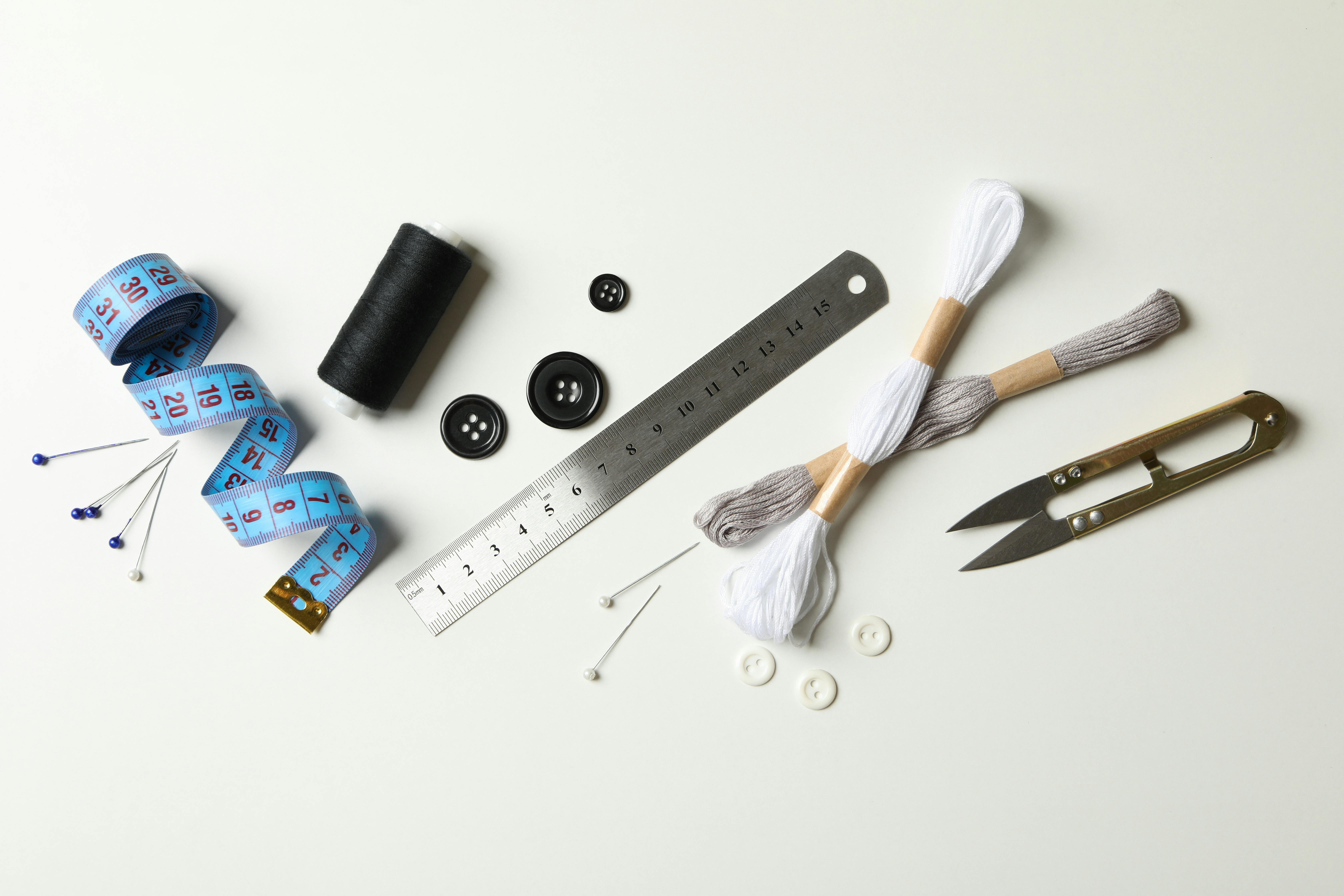  flat lay of sewing tools like pins, measuring tape, buttons, thread and snips