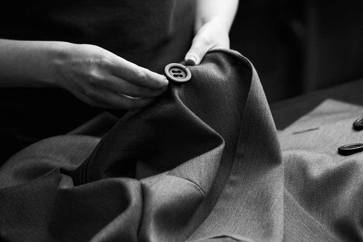 Hands sewing a button onto a tailored jacket