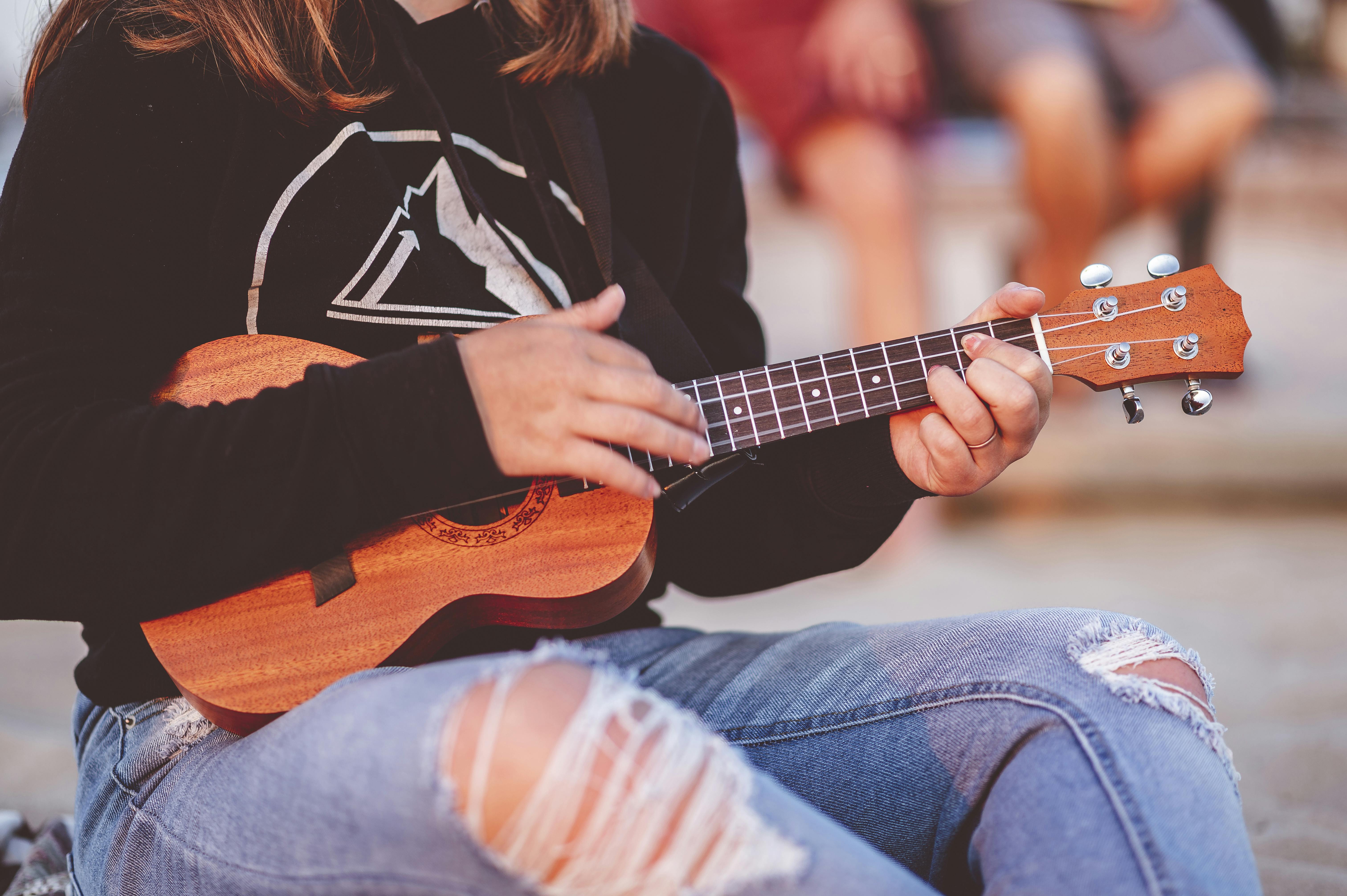  woman playing ukulele with ripped jeans and black sweatshirt
