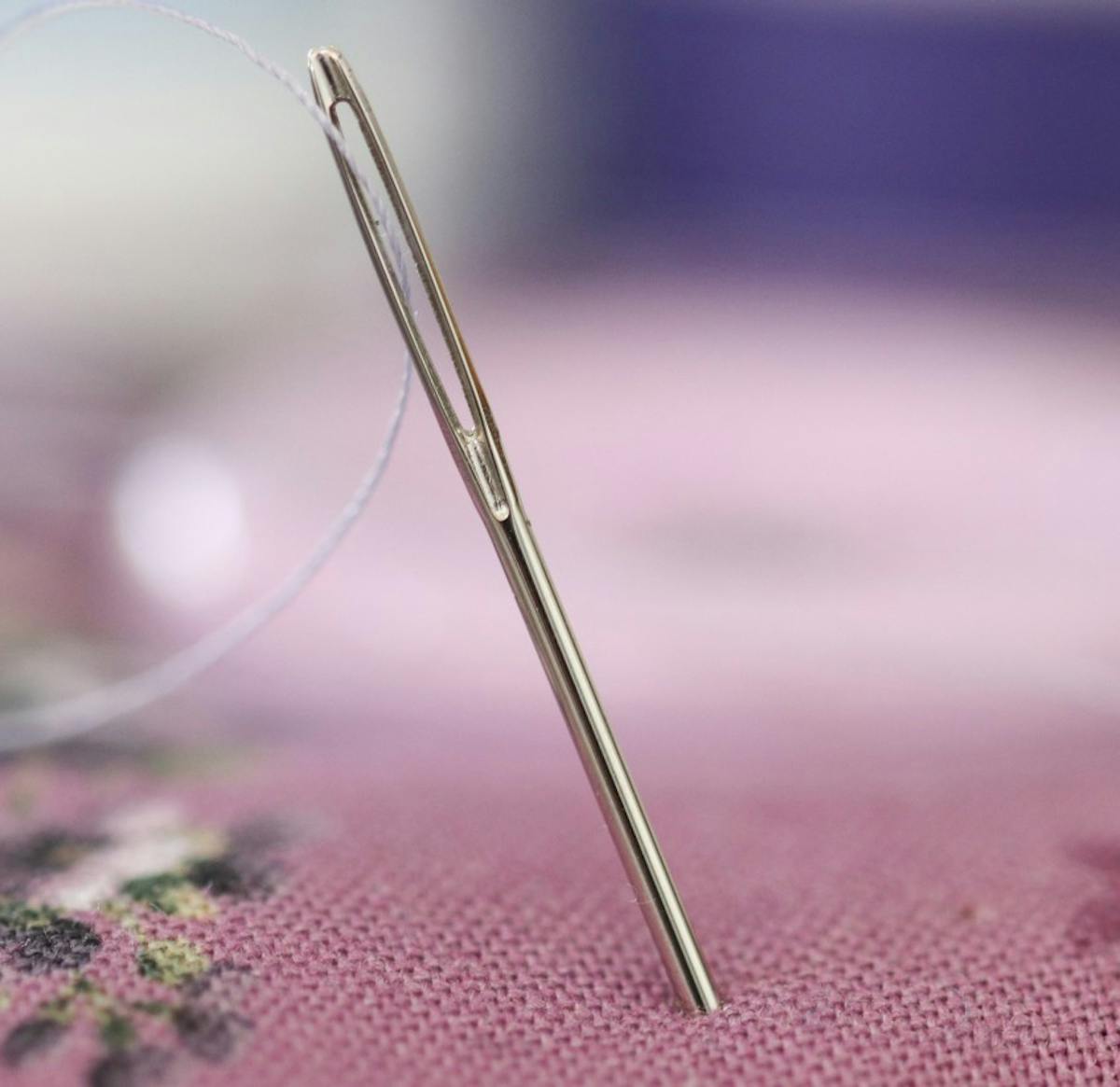  needle in pink pin cushion with thread through the eye of the needle