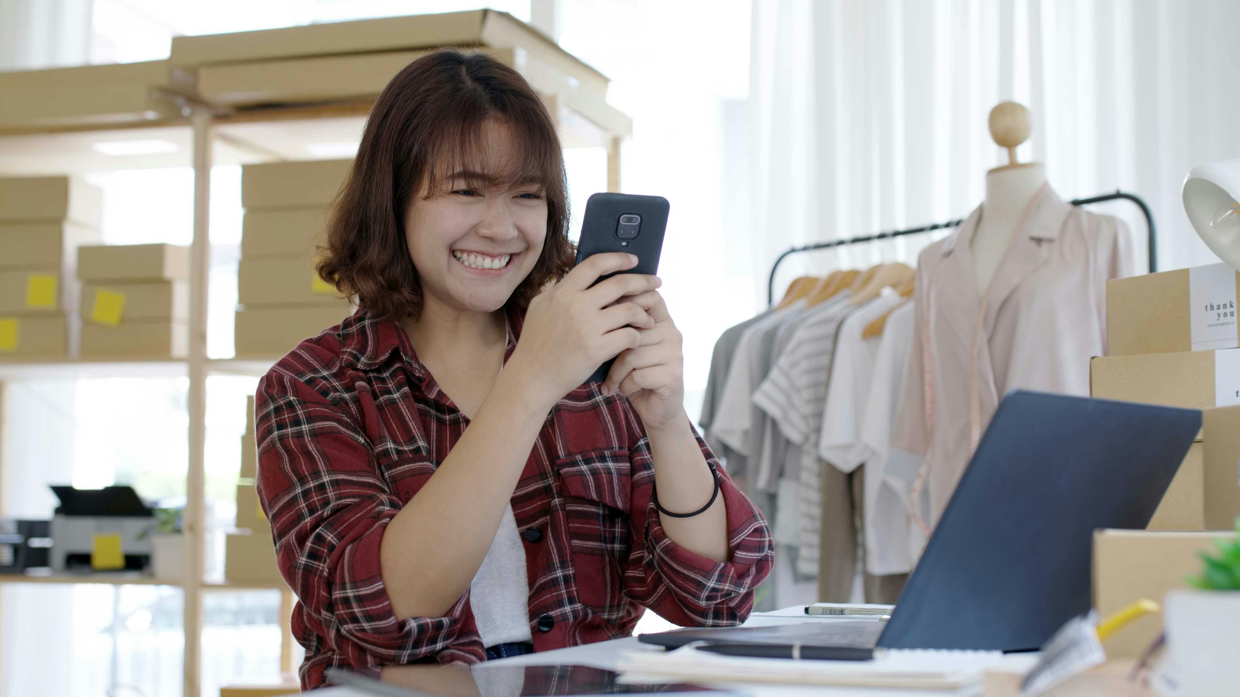  woman smiling at her phone in fashion studio for selling online