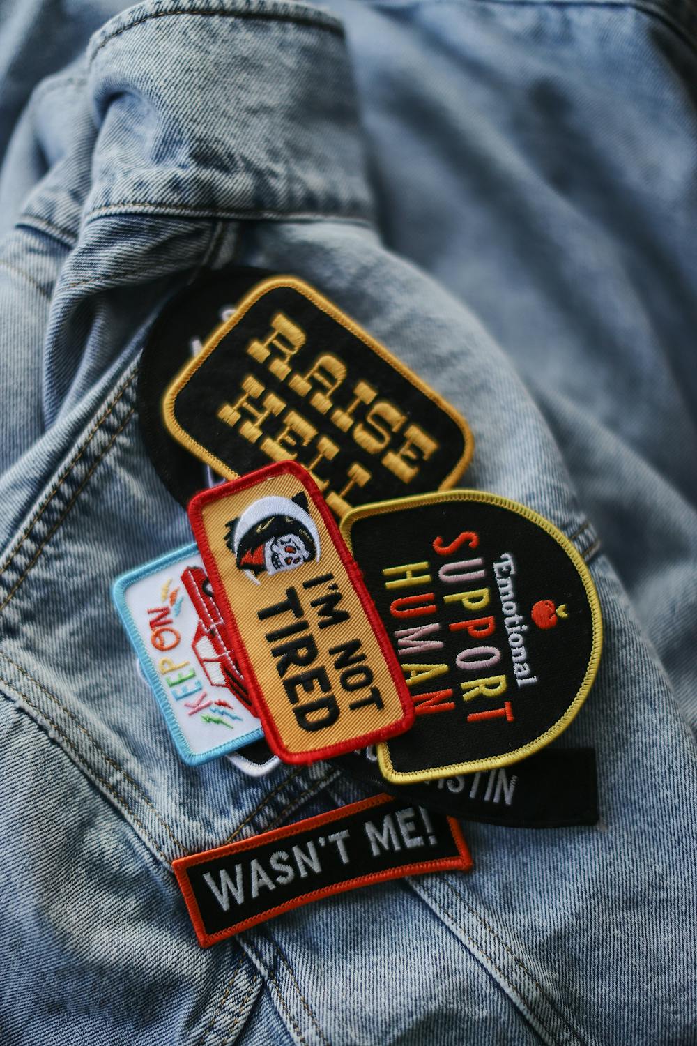 A collection of embroidered patches laid out on a light blue denim jacket A collection of embroidered patches laid out on a light blue denim jacket