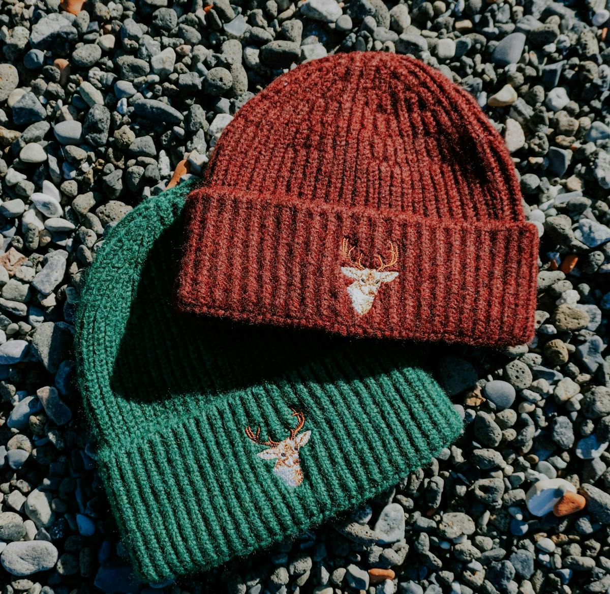 two beanies with embroidered patches on the front laying on the ground two beanies with embroidered patches on the front laying on the ground