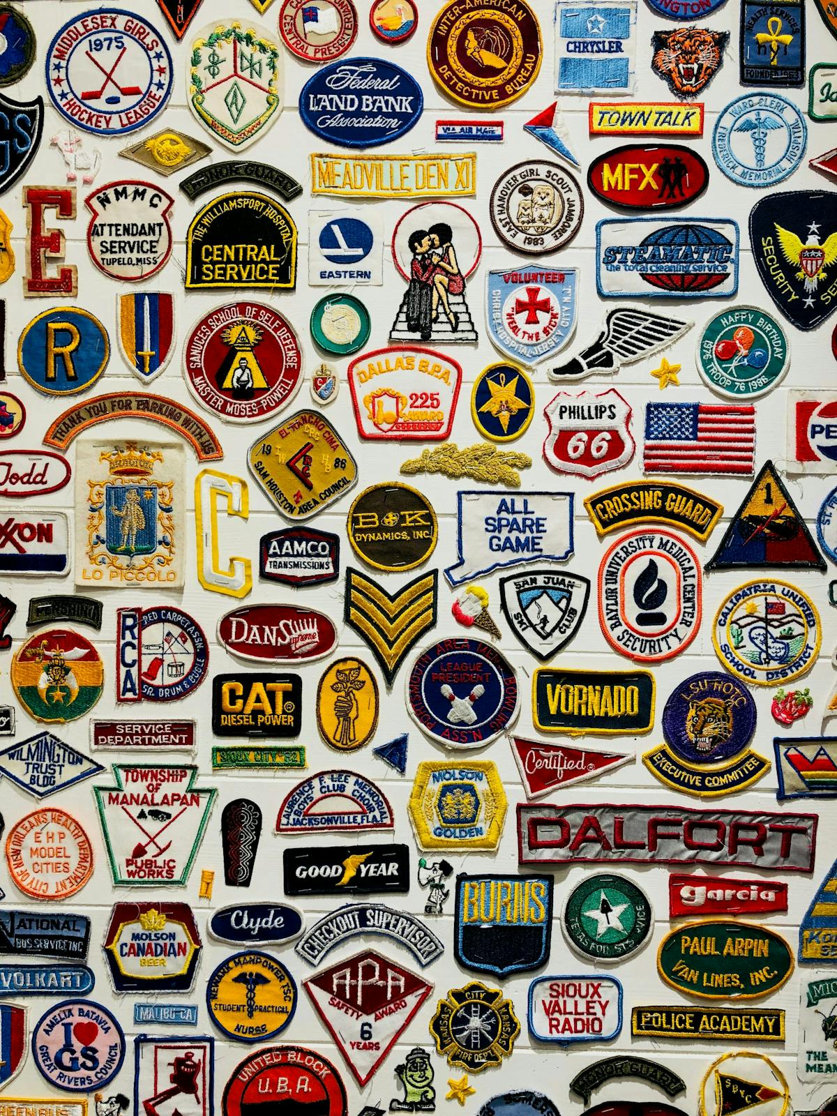 a collection of various patches hanging on a white wall   a collection of various patches hanging on a white wall