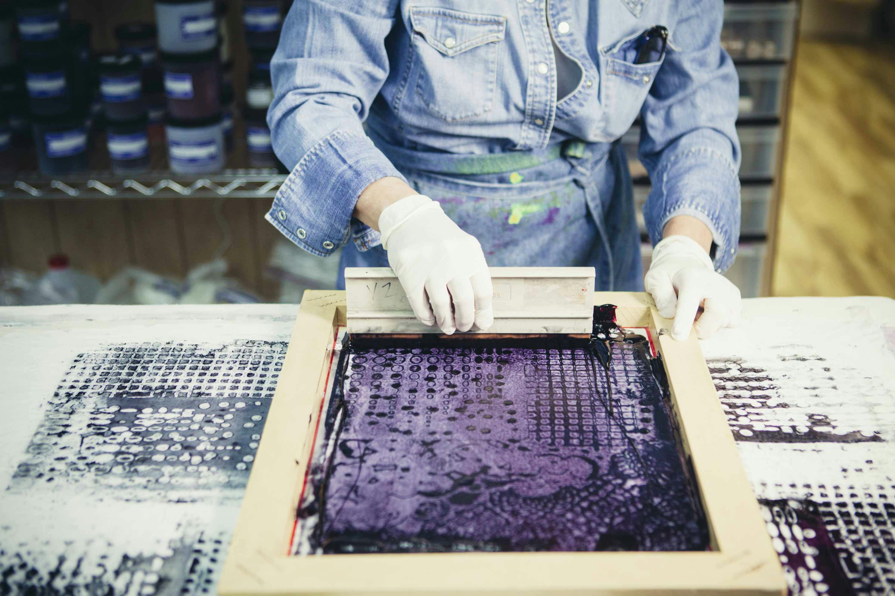  person using a squeegee and silk screen to print textiles