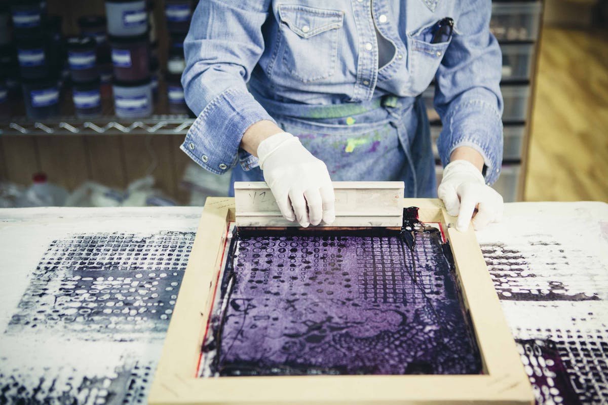 person using a squeegee and silk screen to print textiles person using a squeegee and silk screen to print textiles