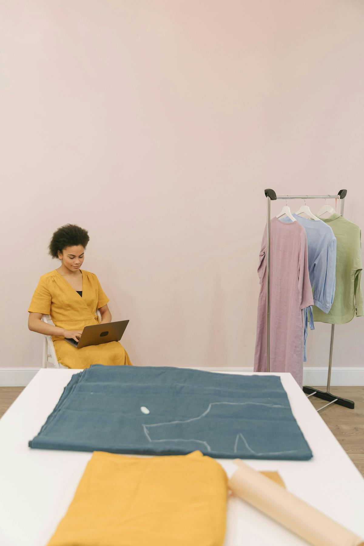 a table with fabric in the front, in the back a woman is sitting on a chair with a laptop on her lap a table with fabric in the front, in the back a woman is sitting on a chair with a laptop on her lap