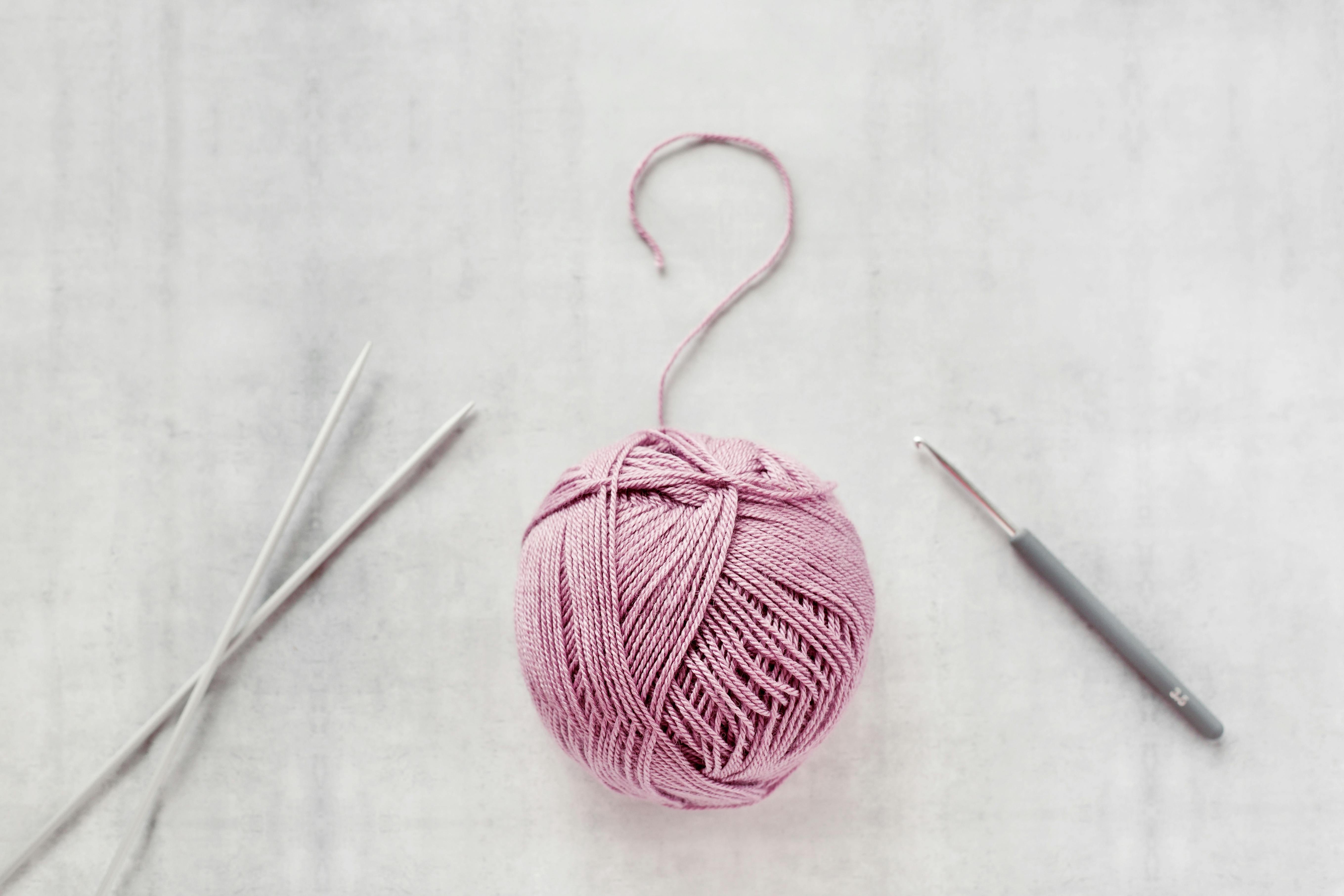 a ball of pink yarn with knitting needles on the left and a crochet hook to the right