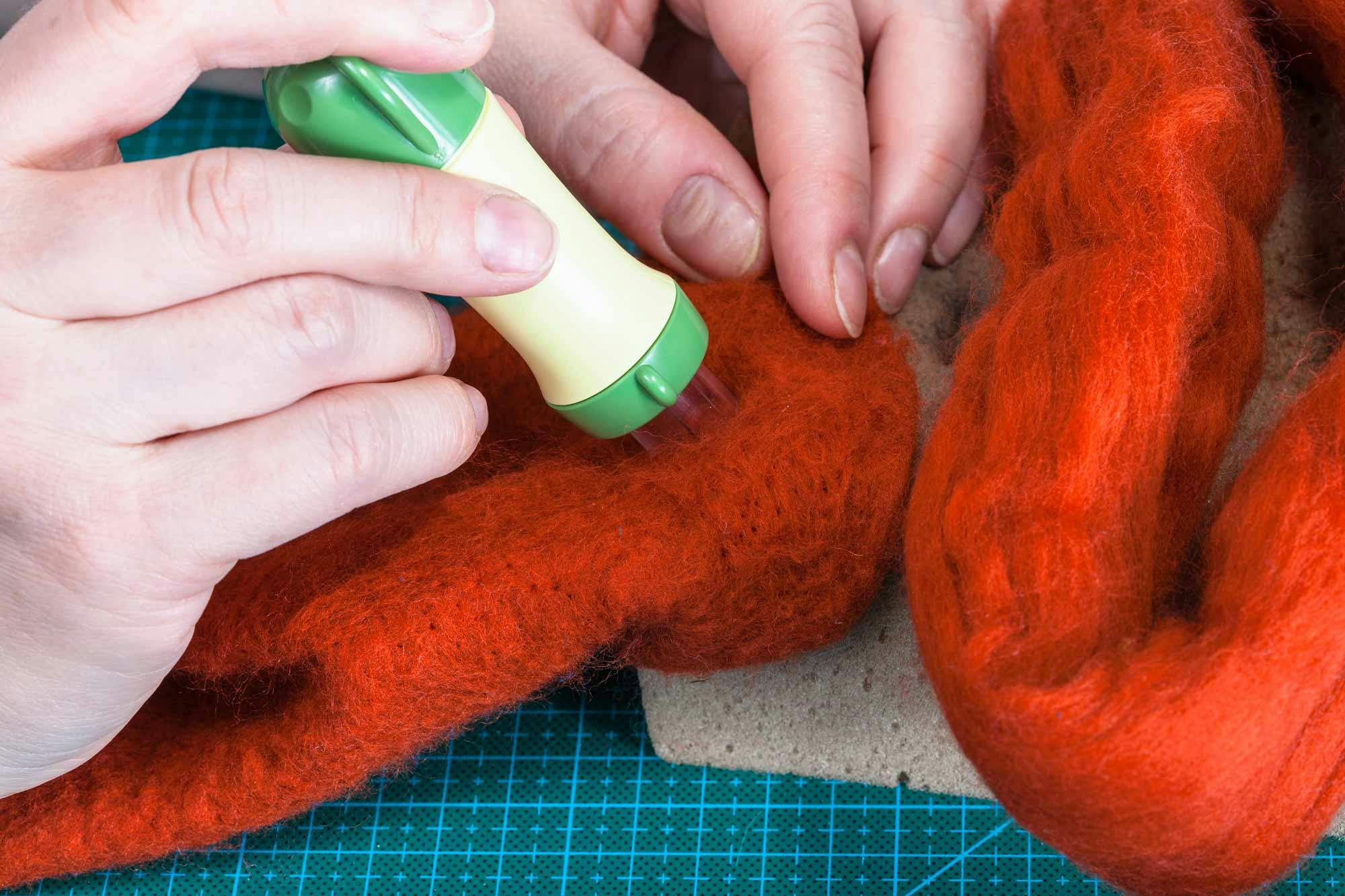  close up of craftsperson using felting needle to create red felt fabric