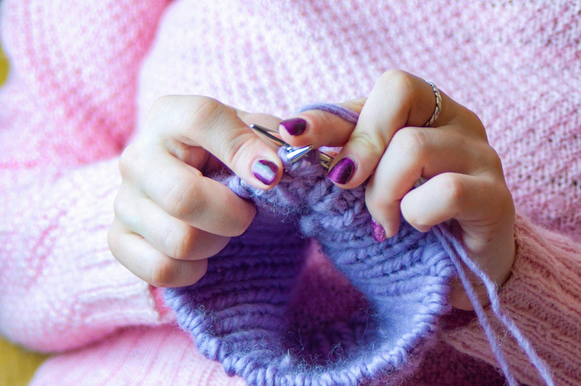  Une femme en train de tricoter un pull en laine violet à la main