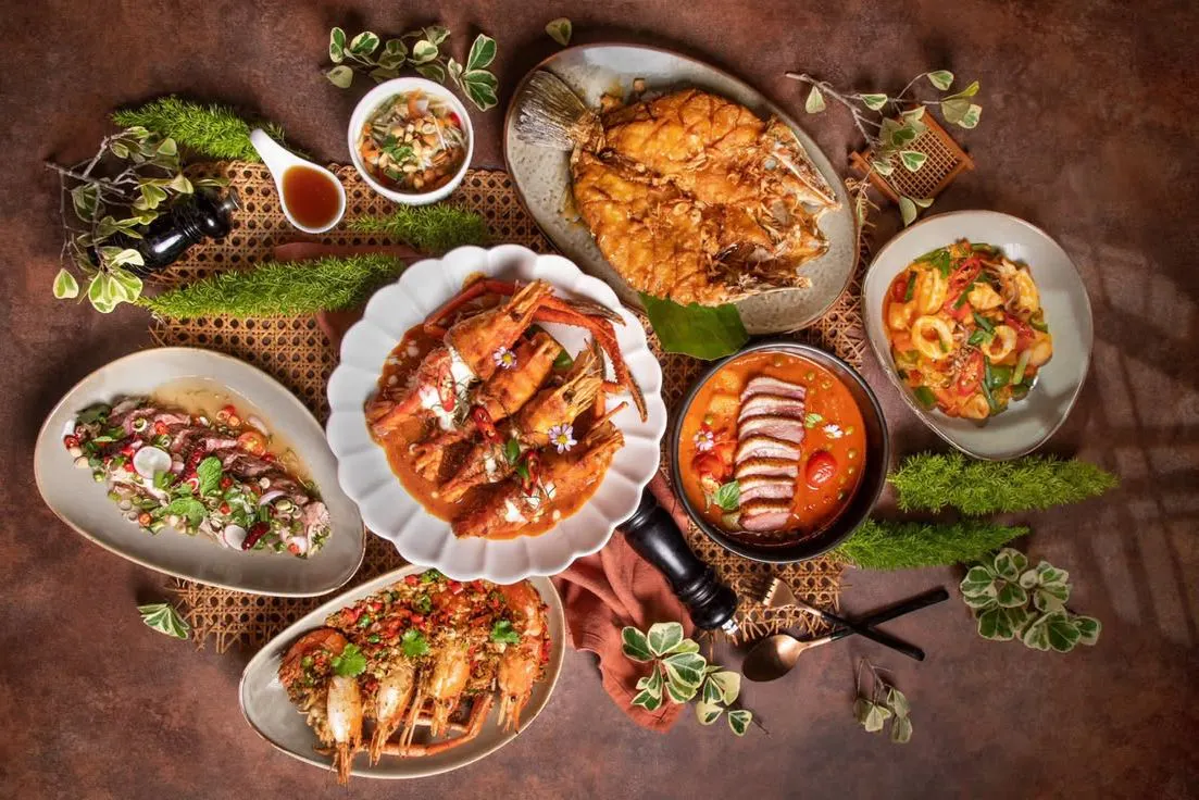 Overhead view of a seafood feast featuring grilled fish, prawns, seafood curry, and other dishes arranged on a restaurant table.