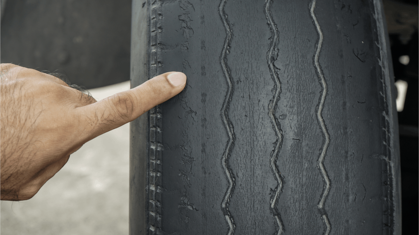 Hand pointing to excessive wear on a car tyre
