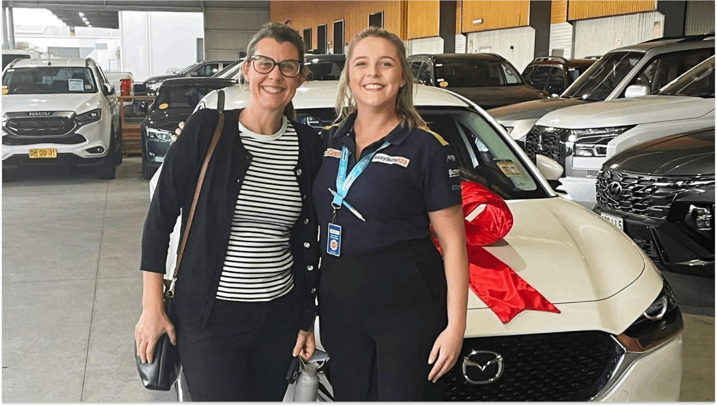 Happy Hendra customer along with easyauto123 salesperson in front of a white Mazda CX-5 and a red bow on the bonnet