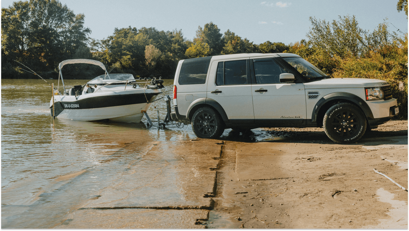 White Landrover towing white power boat out of lake