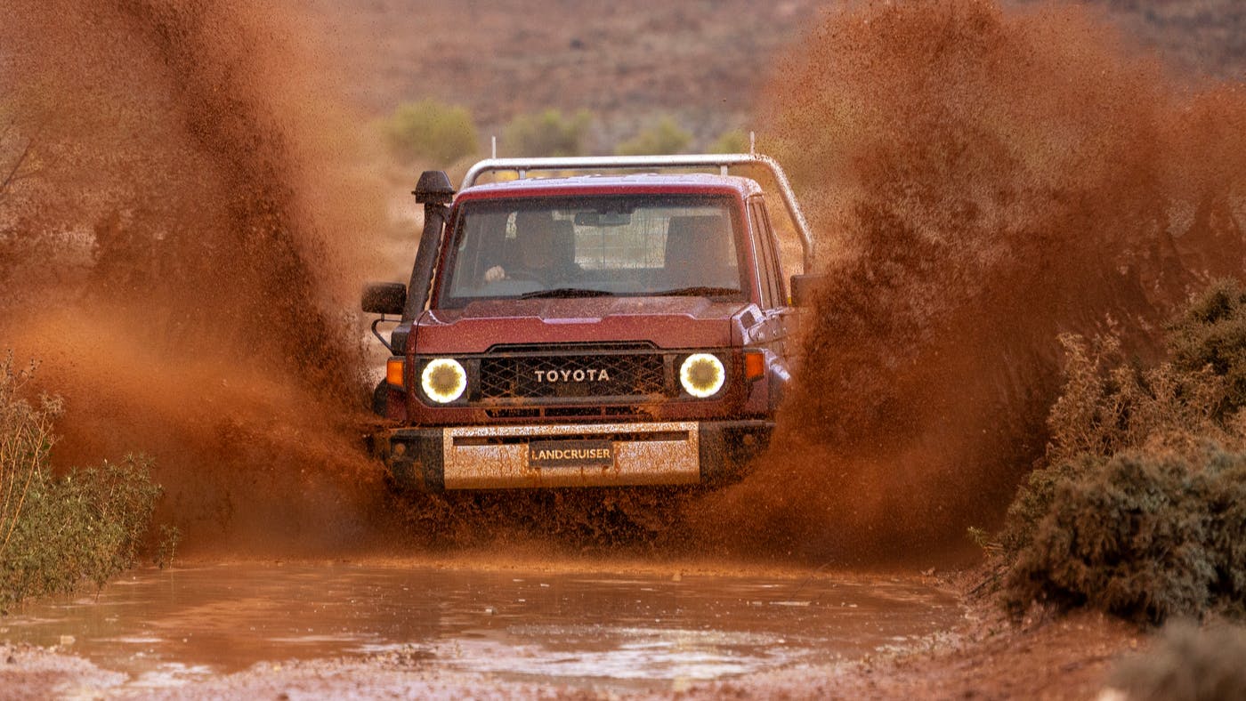 Toyota Landcruiser 70 Series driving through muddy puddle at speed