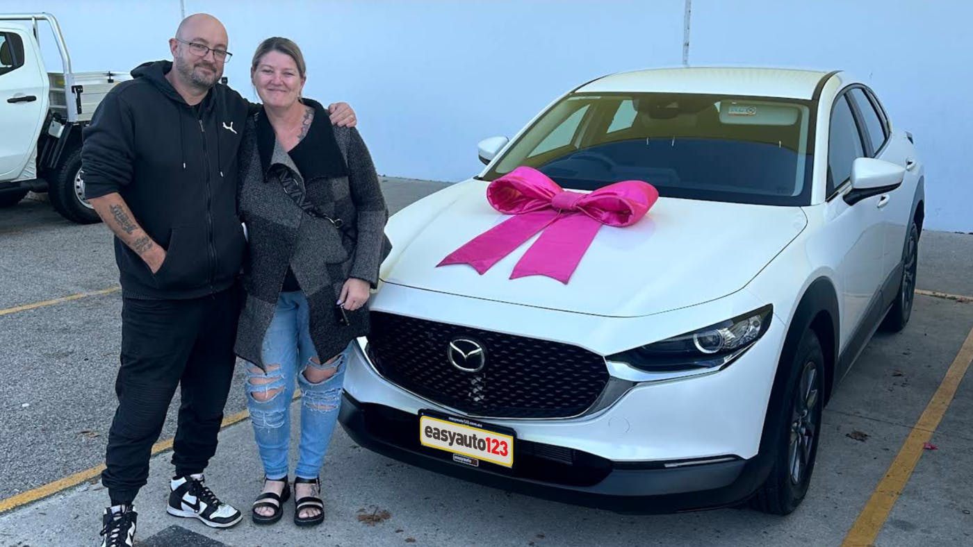 Happy couple stood arm-in-arm by a white SUV with a pink bow outside easyauto123 Joondalup