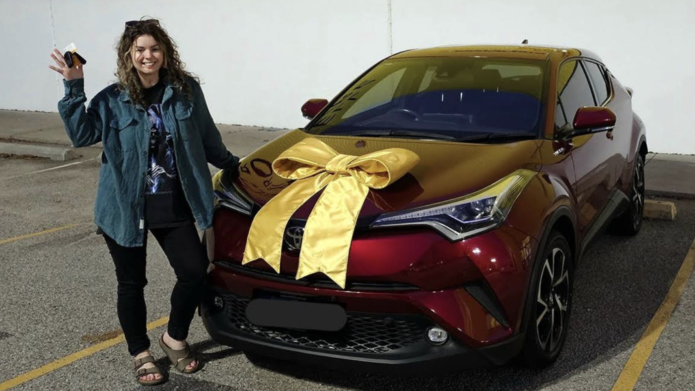 Young woman smiling and holding keys stood by a dark red SUV with a yellow bow outside easyauto123 Joondalup