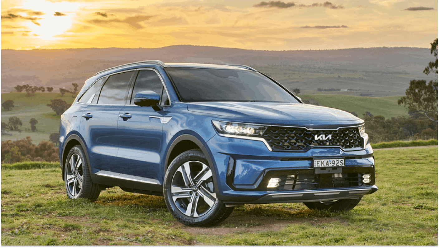 Blue Kia Sorento parked in field with hils in background and golden sunset