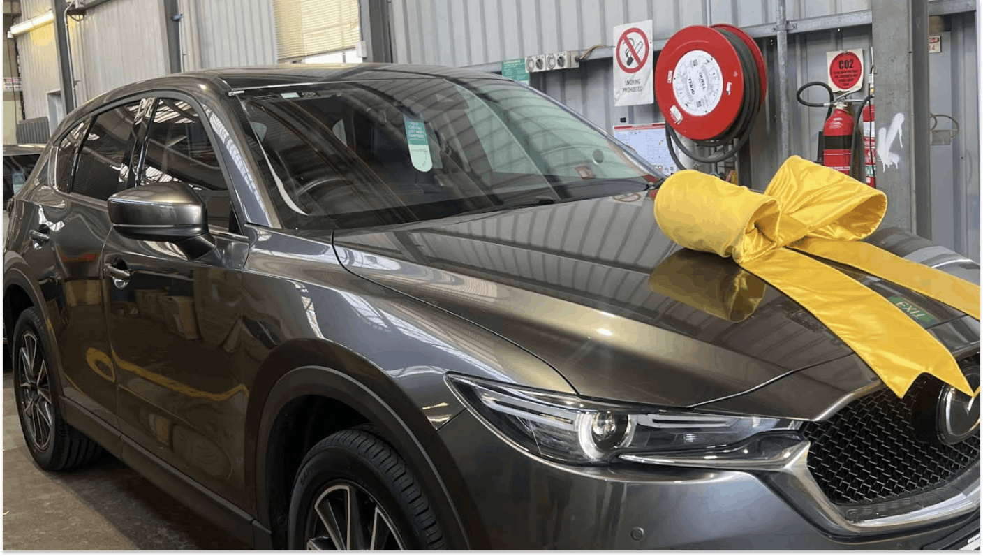 Silver Mazda in used car warehouse with big yellow bow on the bonnet