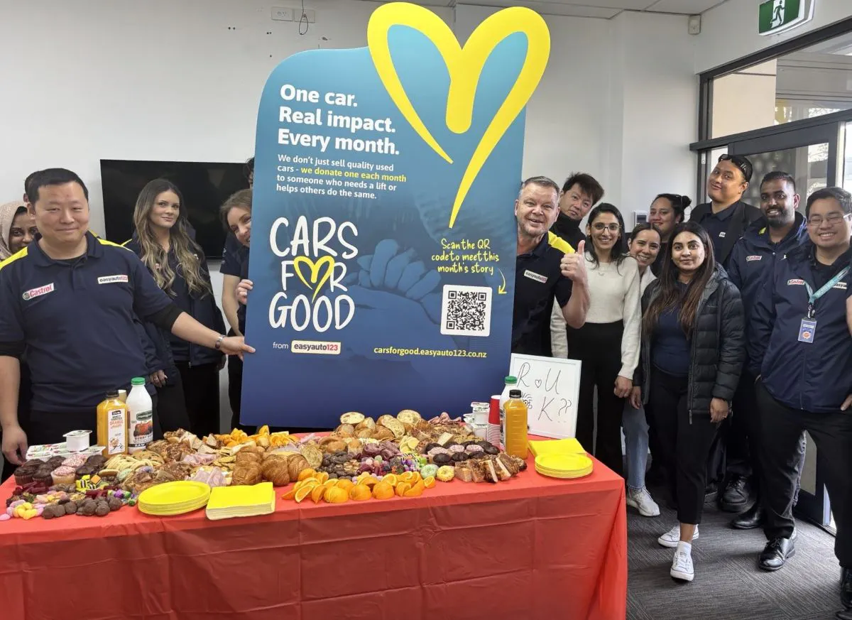 A group of easyauto123 staff in New Zealand gathered around a Cars for Good banner with morning tea in the foreground