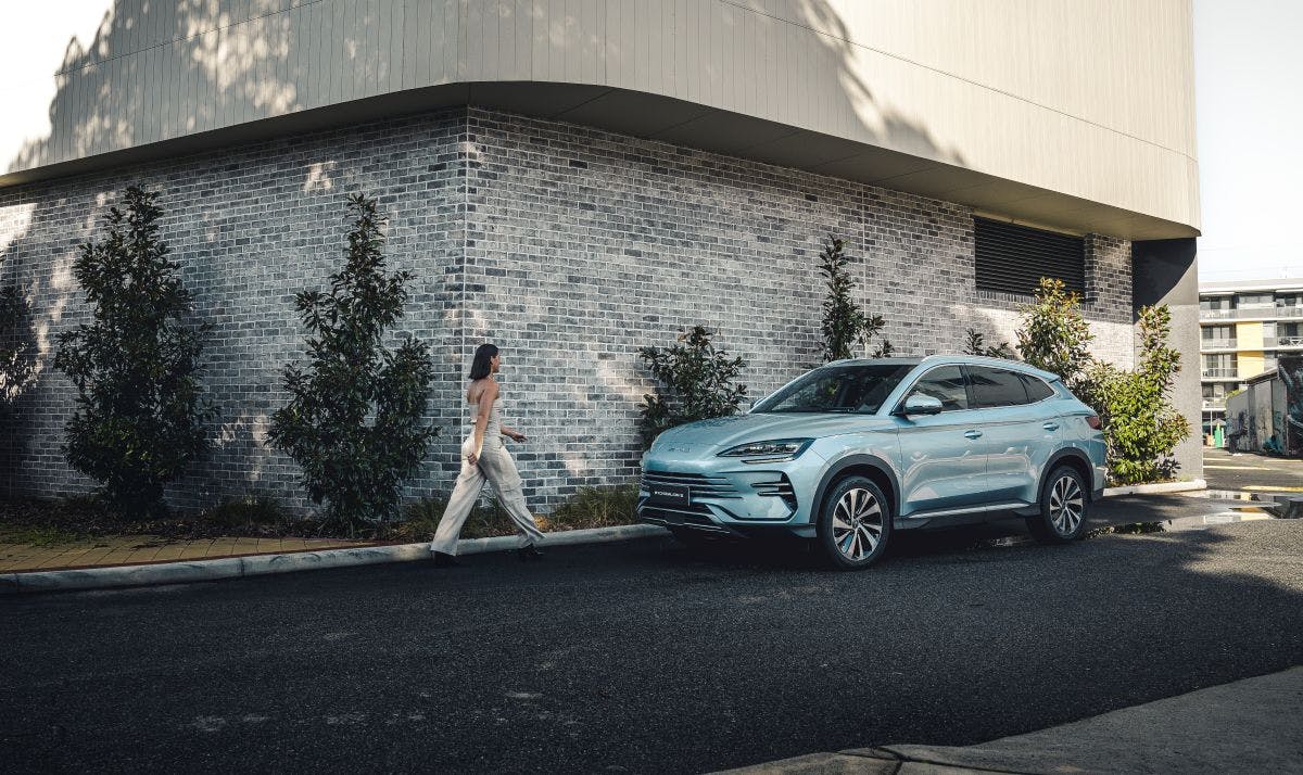 A woman walking purposefully down the street towards an electric car.