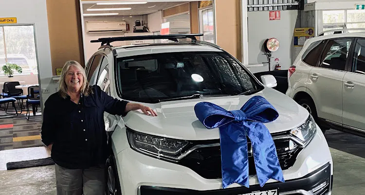 Woman proudly smiling next to her used car
