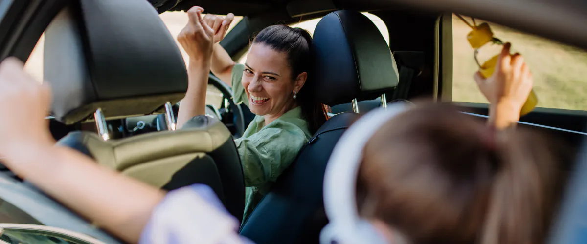 Young mother in driver's seat of car laughing and entertaining her child in the back seat