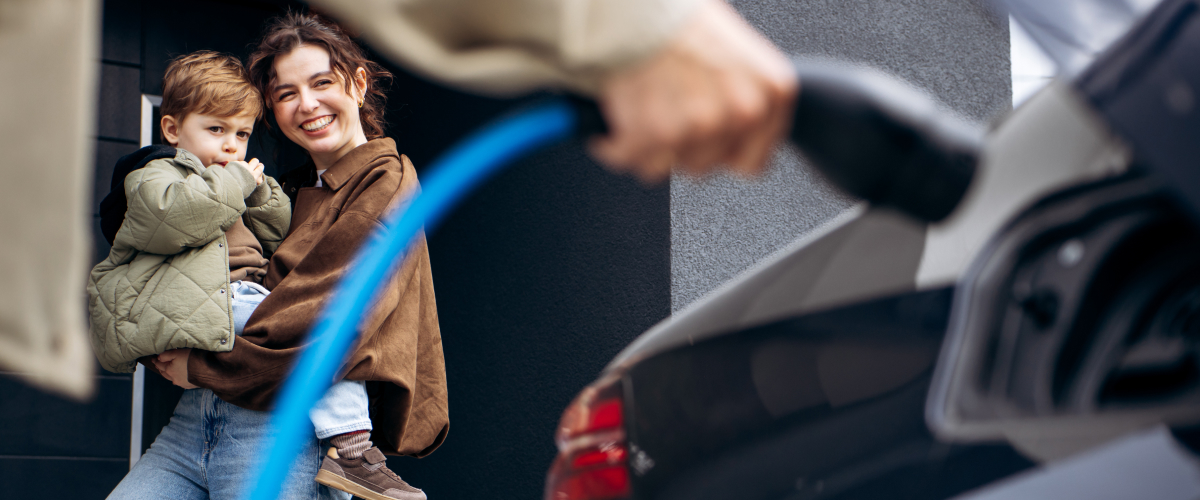 Mother holding young boy watching husband plug EV charger into car